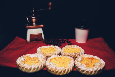 A small personal size fruit filled pie in a tinfoil dish on a wood table top illuminated with...