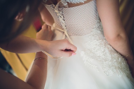 Bridesmaid tying a bow on a bride's elegant wedding dressの写真素材