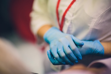 Close up of female doctor's hands putting on blue sterilized surgical gloves in the office