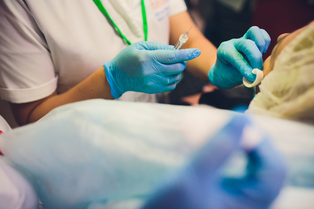 Close up of female doctor's hands putting on blue sterilized surgical gloves in the office holding syringeの写真素材