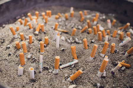 Dirty steel ashtray full of old cigarette and cigar butts - isolated on whiteの写真素材