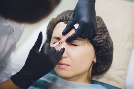 Cosmetologist doctor make facial beauty injections to her woman client. Beautiful female face and cosmetologists hands with syringe. Rejuvenation and hydratation. Cosmetology concept in clinic.の写真素材
