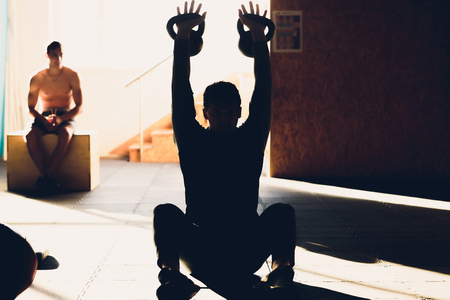 Young man lifting dumbbell and kettlebell at the fitness center.の写真素材