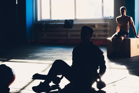 Young man lifting dumbbell and kettlebell at the fitness center.