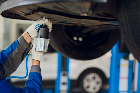 Young mechanic fixing wheel under car in serviceの写真素材