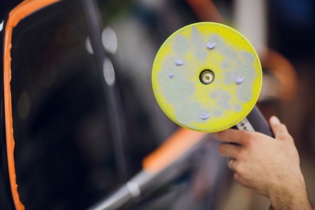 A man in a special suit polishes a gray car body, a tool for polishing cars, into a workshop.の写真素材
