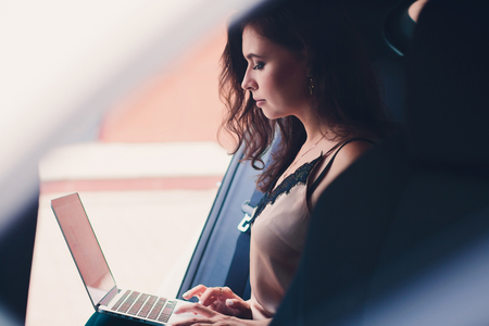 Business woman sitting in the back seat of an elite car holding a laptop.の写真素材