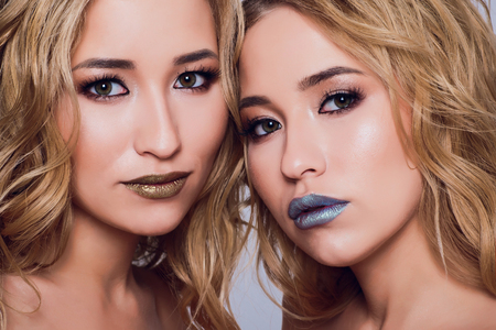 Two beautiful women in black night fashion dress posing isolated on a white gray background. Pretty brunette girl friends twins having fun drinking cocktails. Singing and dancing. Festive mood. Insideの写真素材