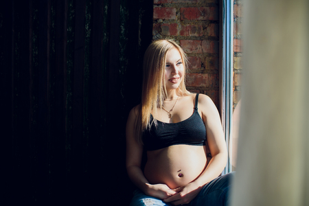 Young beautiful pregnant woman sitting on windowsill at homeの写真素材