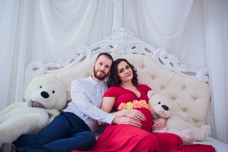 Young family prepares to become parents. Husband gently hugs his pregnant wife at home on the couch....