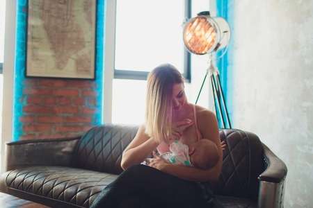 breastfeeding Woman breast feeding baby in modern loft interior. Minimalistic scandinavian design. young mother in sportswear, workout at home.の写真素材