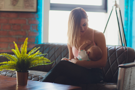 Woman breast feeding baby in modern loft interior. Minimalistic scandinavian design. young mother in sportswear, workout at home.の写真素材
