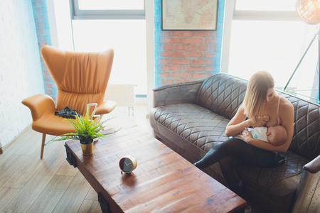 breastfeeding Woman breast feeding baby in modern loft interior. Minimalistic scandinavian design. young mother in sportswear, workout at home.の写真素材