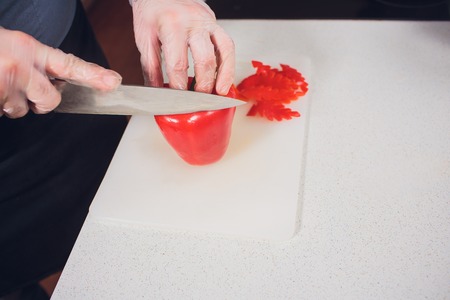 Slicing sweet red pepper on cutting board. male hand cuts capsicum with knife. View from aboveの写真素材