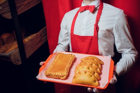 Baker keeps a tray with fresh bread man in red and white uniform baker holding a tray with bread makingの写真素材