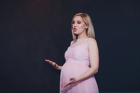 Casually dressed attractive pregnant woman standing home, looking camera and smiling whilstの写真素材