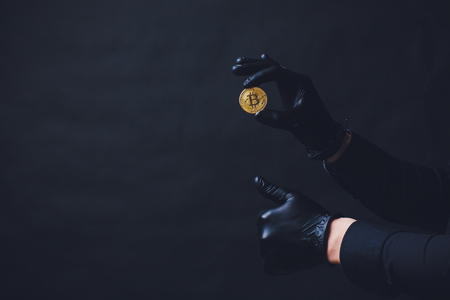 Bitcoins placed on arm Hands in black gloves show symbol. Isolated on black backgroundの写真素材