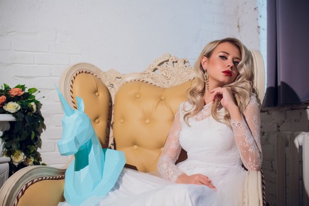 Freaky blonde girl and unicorn head mask. Fantasy unicorn keep calm with girlfriend. Unusual young people sits together.の写真素材