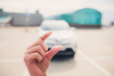 Female holding transparent heart shaped object with car on background.の写真素材