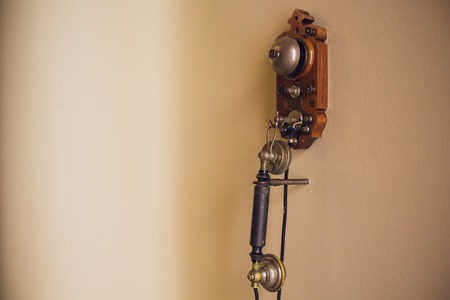 Old retro wood telephone on a beige white wall.