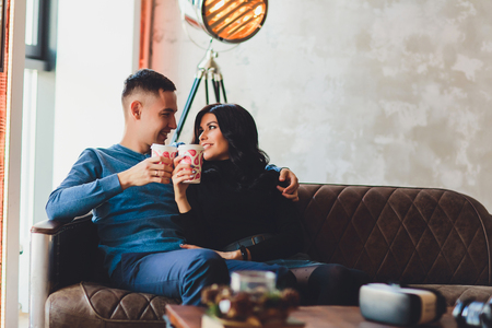 Beautiful couple sitting at romantic atmosphere looking each other, talking, smiling and drinking warm tea. Pregnant wife and her husband spanding time together at kitchen. Pragnancy family concept.の写真素材