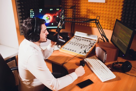 Portrait of radio host using sound mixer on table in studio.