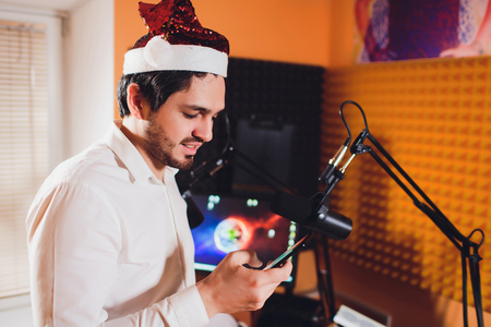 Portrait of radio host using sound mixer on table in studio. Santa Claus hatの写真素材