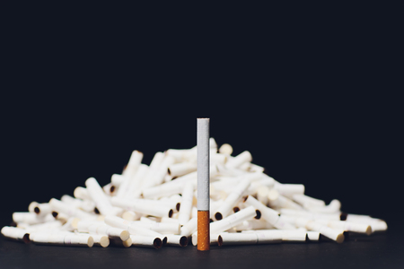 Newest electronic cigarettes, heating tobacco system IQOS, smoking, dark blue isolated on black background mountain of used cigarettes, sticks classic cigarette on the background of new sticksの写真素材