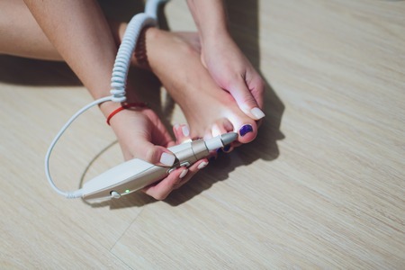 A woman polishing her leg with polish machine at homeの写真素材