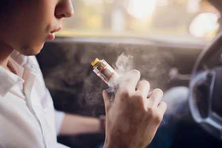 View from the side of a young man smoking an e-cigarette as he drives his car on an urban streetの写真素材