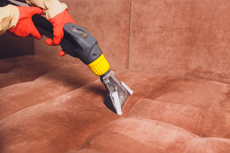 Sofa chemical cleaning with professionally extraction method. Upholstered furniture. Early spring cleaning or regular clean up. Dry cleaner's in light red protective glove employee removing dirt from furniture in flatの写真素材