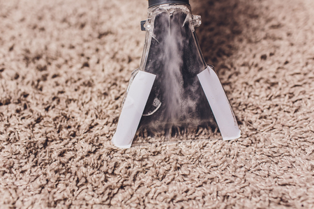Woman removing dirt from carpet with vacuum cleaner in roomの写真素材