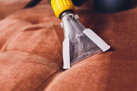 Sofa chemical cleaning with professionally extraction method. Upholstered furniture. Early spring cleaning or regular clean up. Dry cleaner's in light red protective glove employee removing dirt from furniture in flatの写真素材