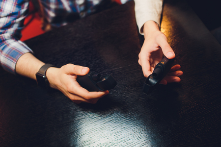 IQOS heat-not-burn tobacco product technology. Two Man holding e-cigarette in his hand before...