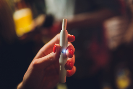 Electronic cigarettes, technology cigarette. Tobacco system IQOS. Female hand on blurred background of the restaurant.の写真素材