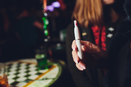 Electronic cigarettes, technology cigarette. Tobacco system IQOS. female hand on blurred background of restaurant.の写真素材