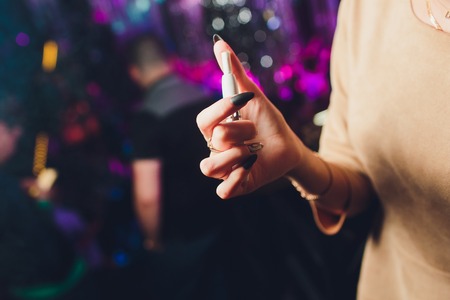 Electronic cigarettes, technology cigarette. Tobacco system IQOS Female hand on blurred background of the restaurant. black case.の写真素材