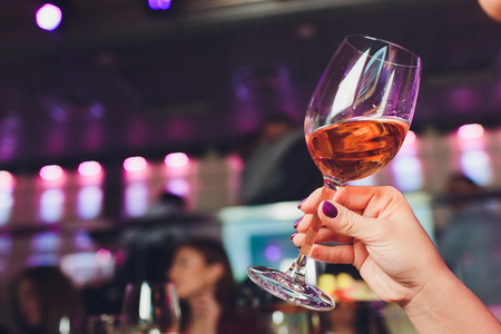 Glass of wine in beautiful female hands. Large glass filled with red wine in woman manicured hands. Concept of romance and celebrationの写真素材