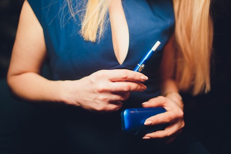 Electronic cigarettes, technology cigarette. Tobacco system IQOS Female hand on blurred background of the restaurant. blue case.の写真素材
