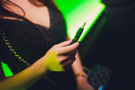 Electronic cigarettes, technology cigarette. Tobacco system IQOS Female hand on blurred background of the restaurant. black case.の写真素材
