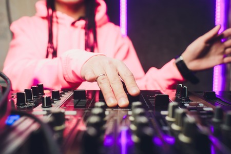 Close up view of the hands of a male disc jockey mixing music on his deck with his hands poised over the vinyl record on the turntable and the control switches at night.の写真素材