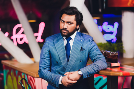 Handsome young man drinking cocktail at bar counter, wearing business suit.