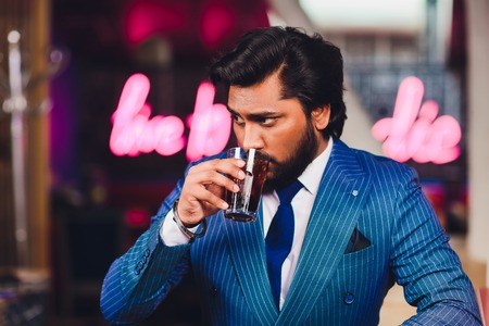Handsome young man drinking cocktail at bar counter, wearing business suit.