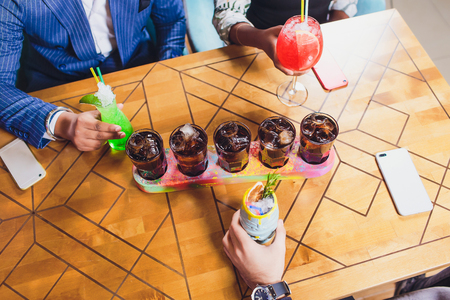 Group of friends drinking cocktails fashion bar restaurants - Side view point of people hands with smartphone - Social gathering concept with addicted men and women - Vivid vintage filter with halo.の写真素材
