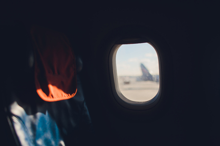 Airplane seat and window inside an aircraft with view of clouds.