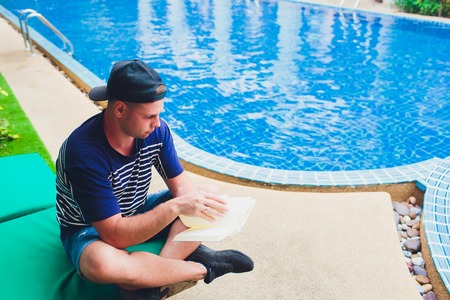 A man reading book beside swimming pool in the garden.