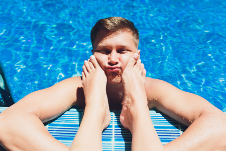 man, female legs, swimming pool, feet on face, henpecked concept.の写真素材