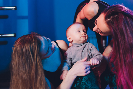 Two young women with dyed red hair and in casual clothes with a baby. Same-sex marriage and adoption.の写真素材