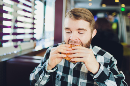 Young man biting fresh tasty hamburger and looking at camera.の写真素材