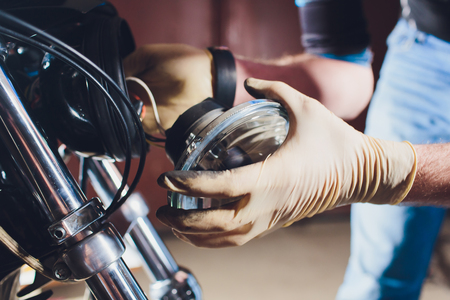 Man fixing bike. Confident young man repairing motorcycle near his garage. replacement lamp in the headlampの写真素材